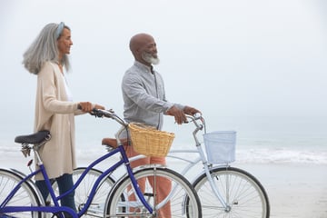 Elderly couple walking on a beach together with bicycles that have baskets while enjoying their retirement years together thanks to investing in an RRSP and TFSA 