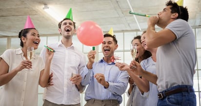 Casual business team celebrating with champagne and party horns in the office