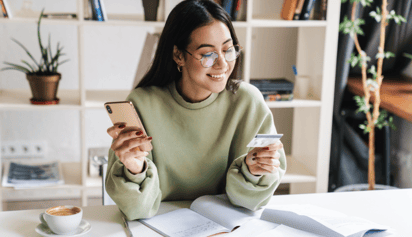 woman looking at her credit card while holding her phone