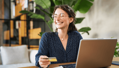 woman wearing glasses holding a credit card and smiling