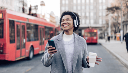 woman wearing headphones and carrying a cup of coffee walking