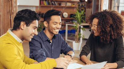 Two men speaking to a woman for free debt help at a table with shelves in the background