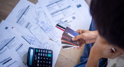 Person holding various credit cards standing over a table covered in bills and a calculator